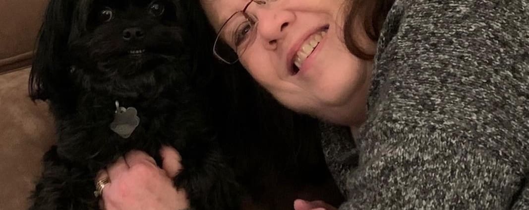 A woman sitting on a couch holding a black dog